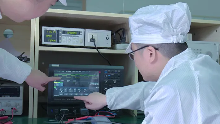 An engineer reviewing a power adapter's switching waveform on a bench oscilloscope during test.