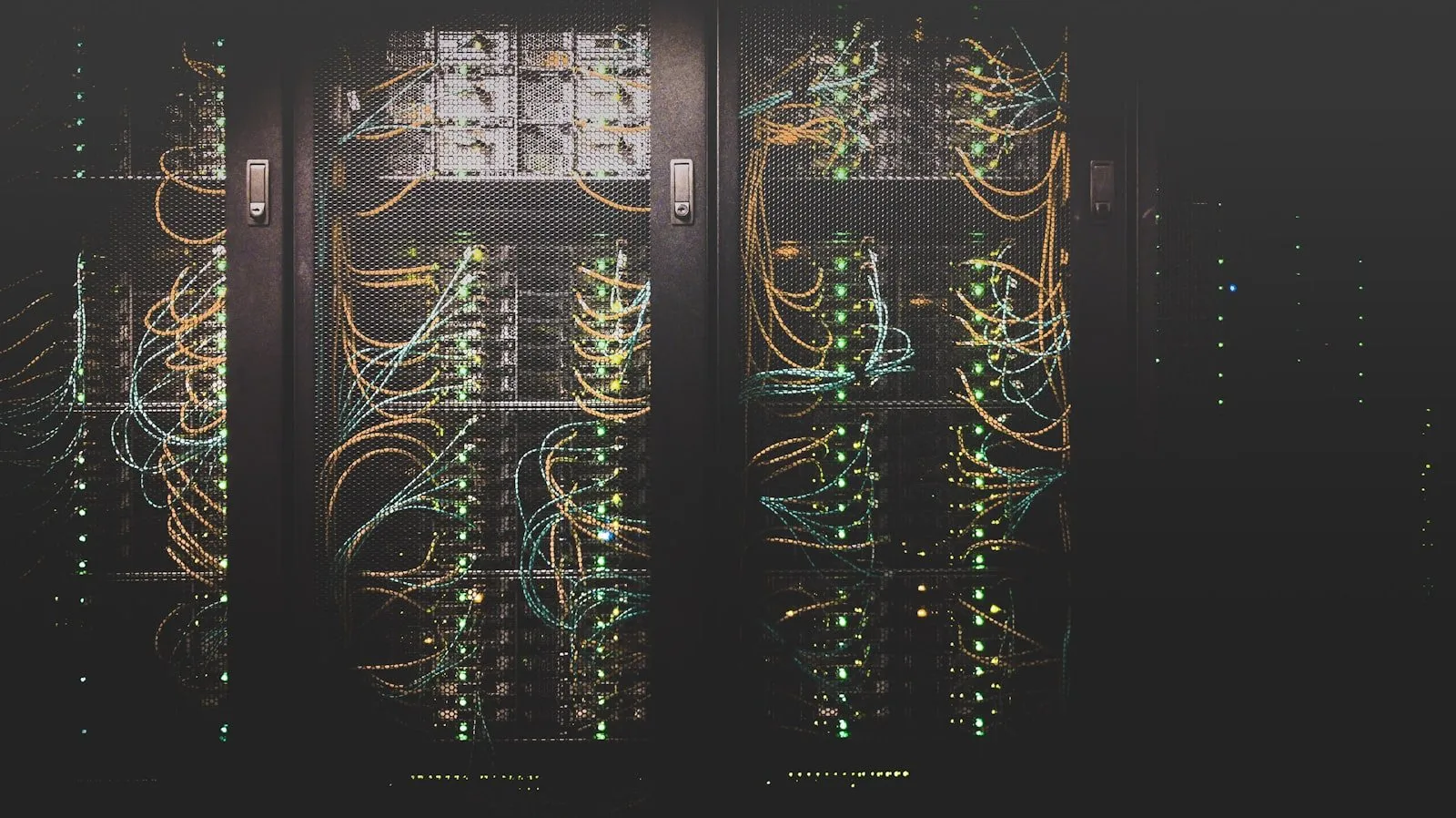 Dark server racks behind mesh doors with dense orange and teal cabling and status LEDs.