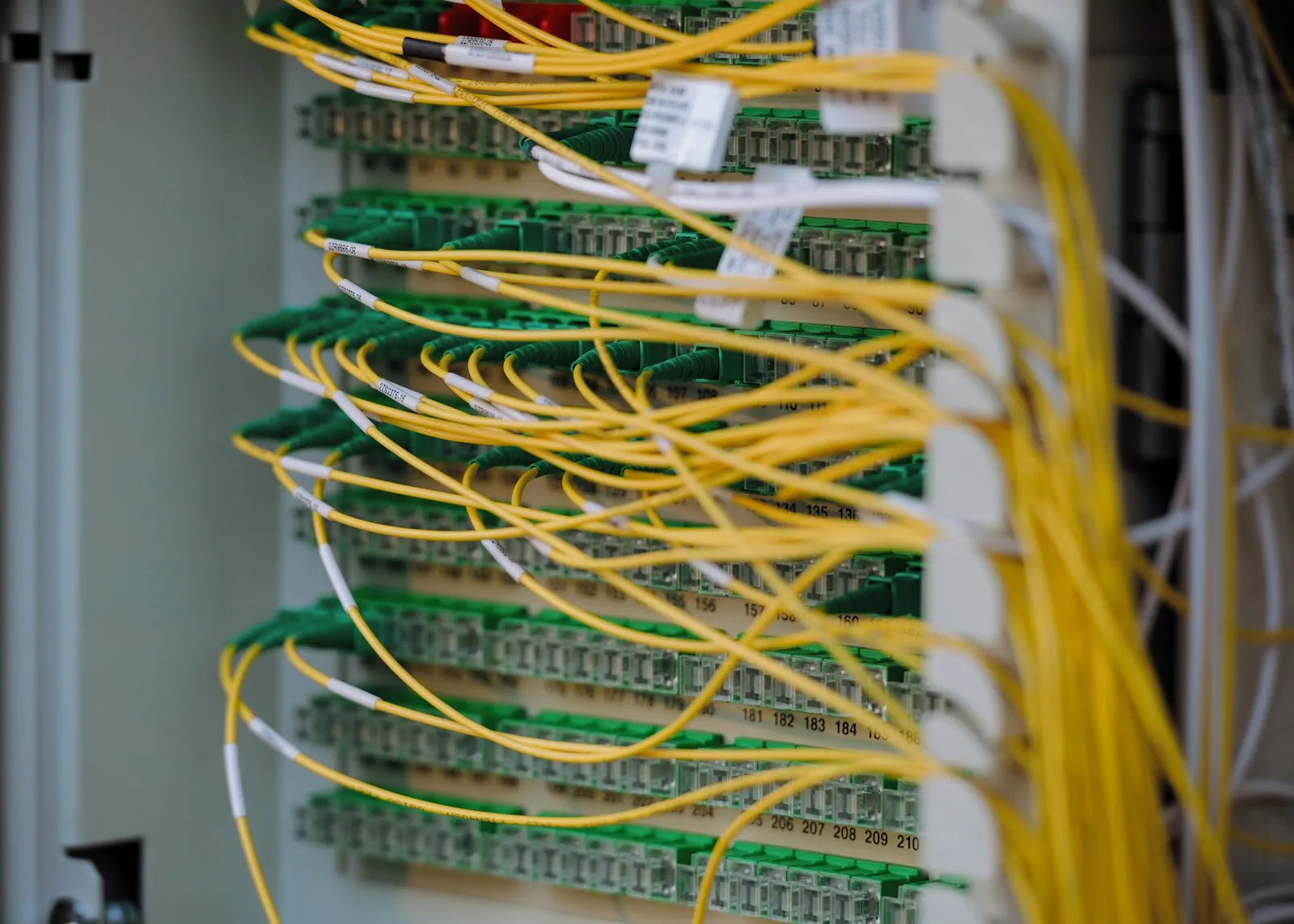Yellow single-mode fiber jumpers with green APC connectors in a numbered optical distribution frame.
