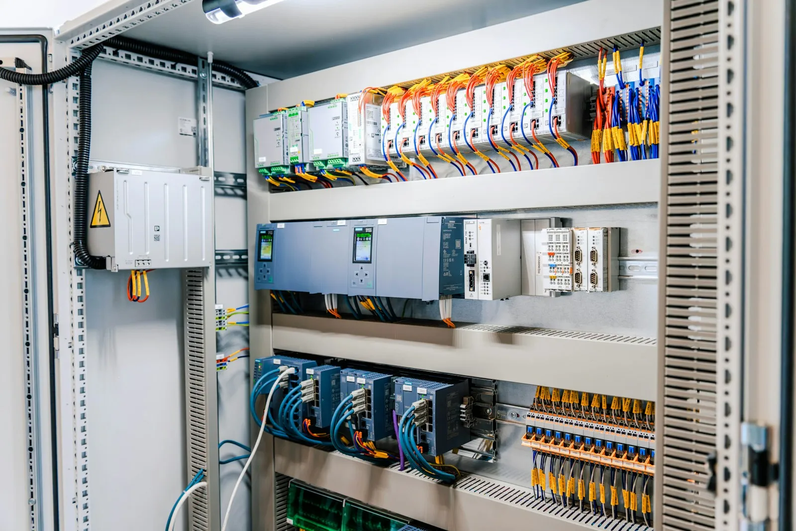 An open industrial control cabinet with DIN-rail modules, wiring, terminal blocks, and breakers.