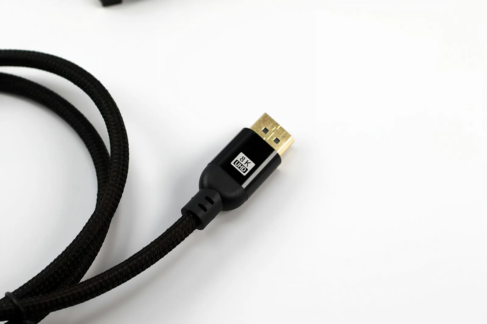 A braided cable with a molded connector and ribbed strain relief on a white surface.