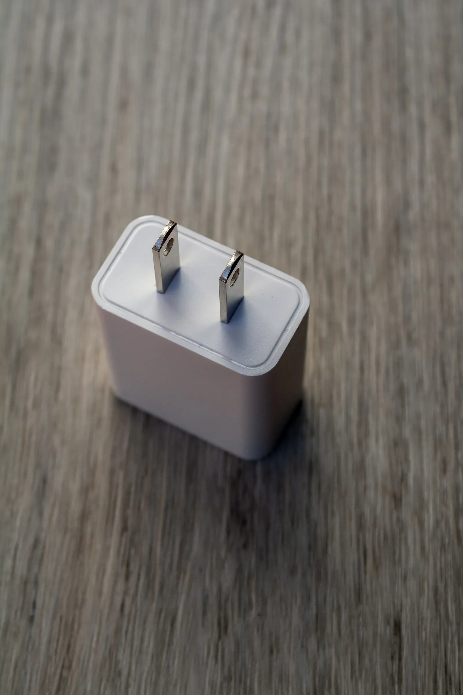 An unbranded white wall-mount power adapter with a US two-prong plug, on a wooden surface.