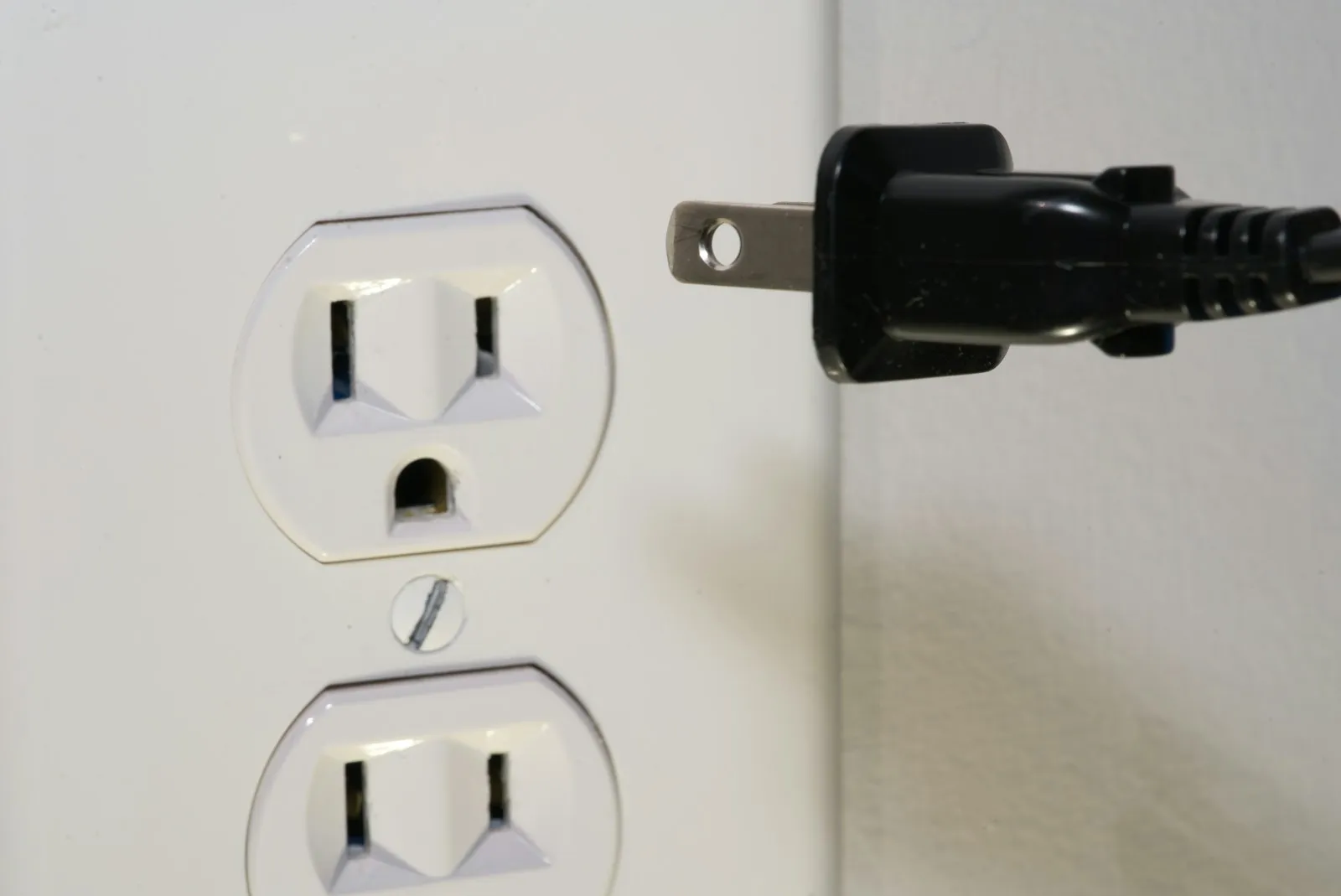 A black NEMA two-prong power plug beside a US wall outlet.