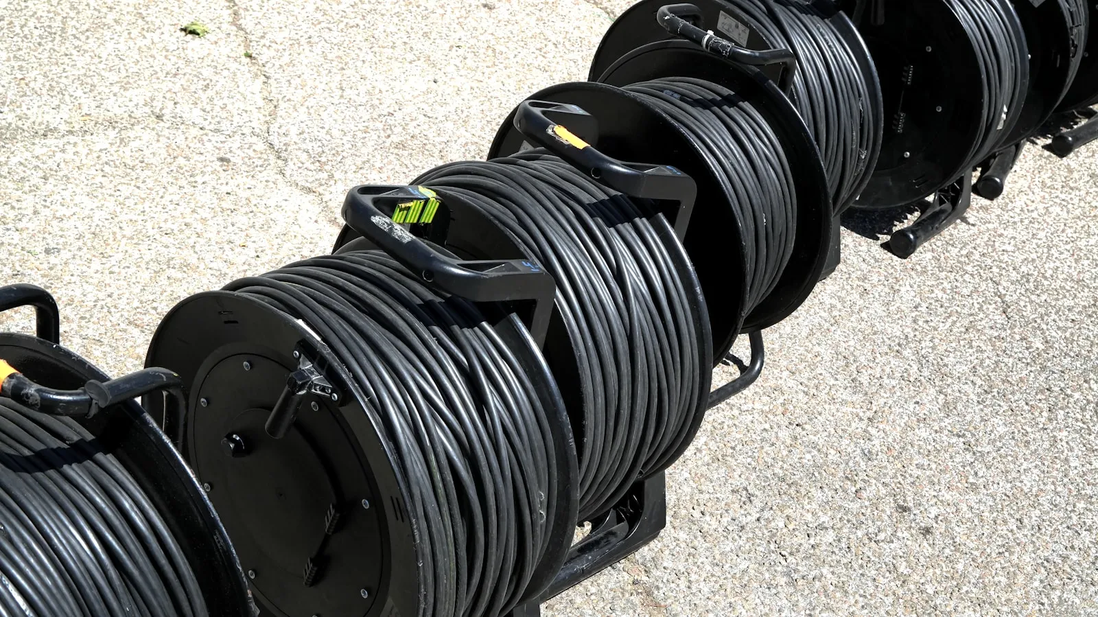 Rows of large spools of black flexible cordage lined up on a floor.