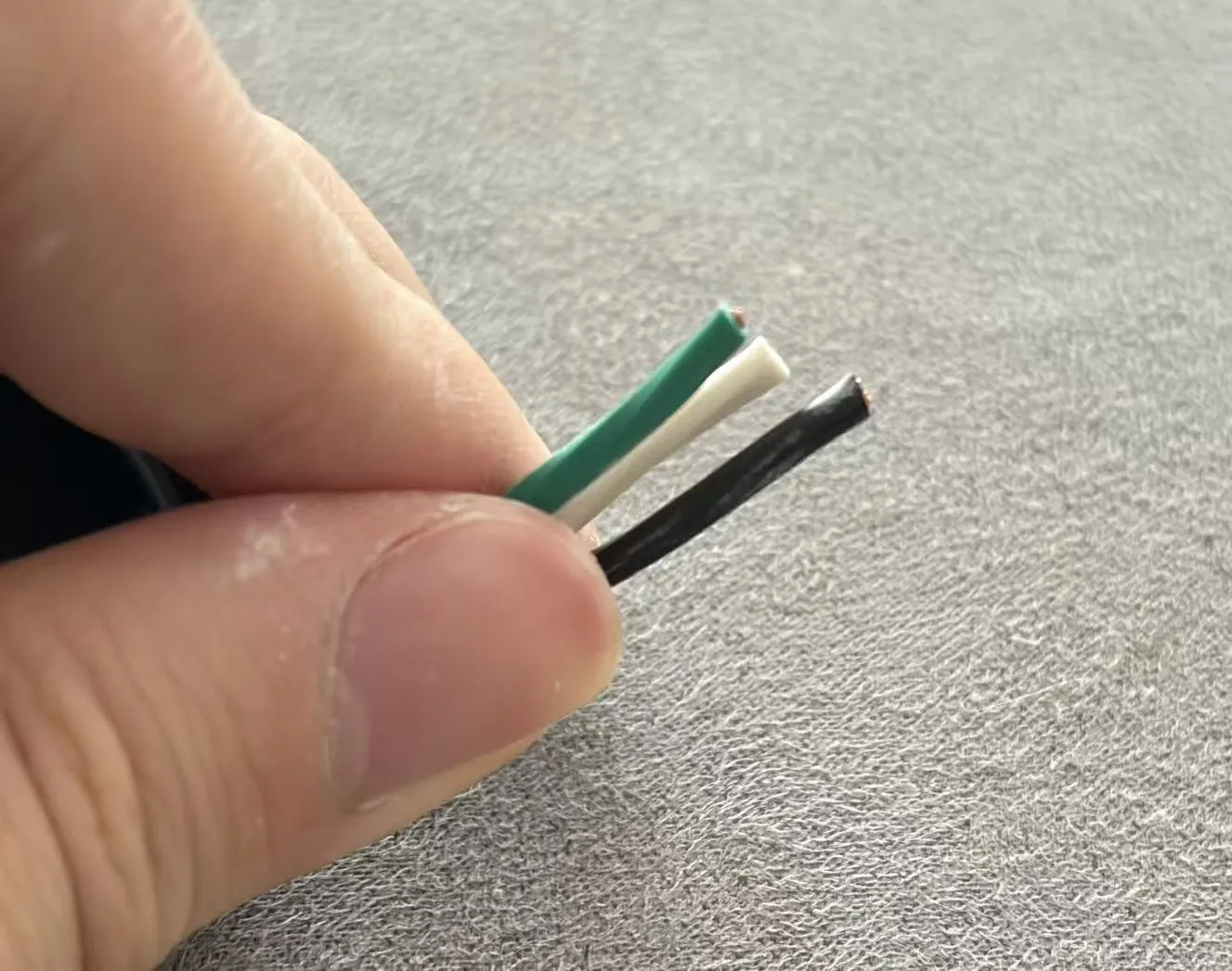 Three stripped conductors from a C13 power cord — green ground, white neutral, black hot — held between fingers.