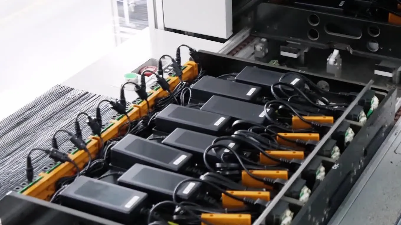 A rack of desktop power adapters wired into an automated test fixture on a production line.