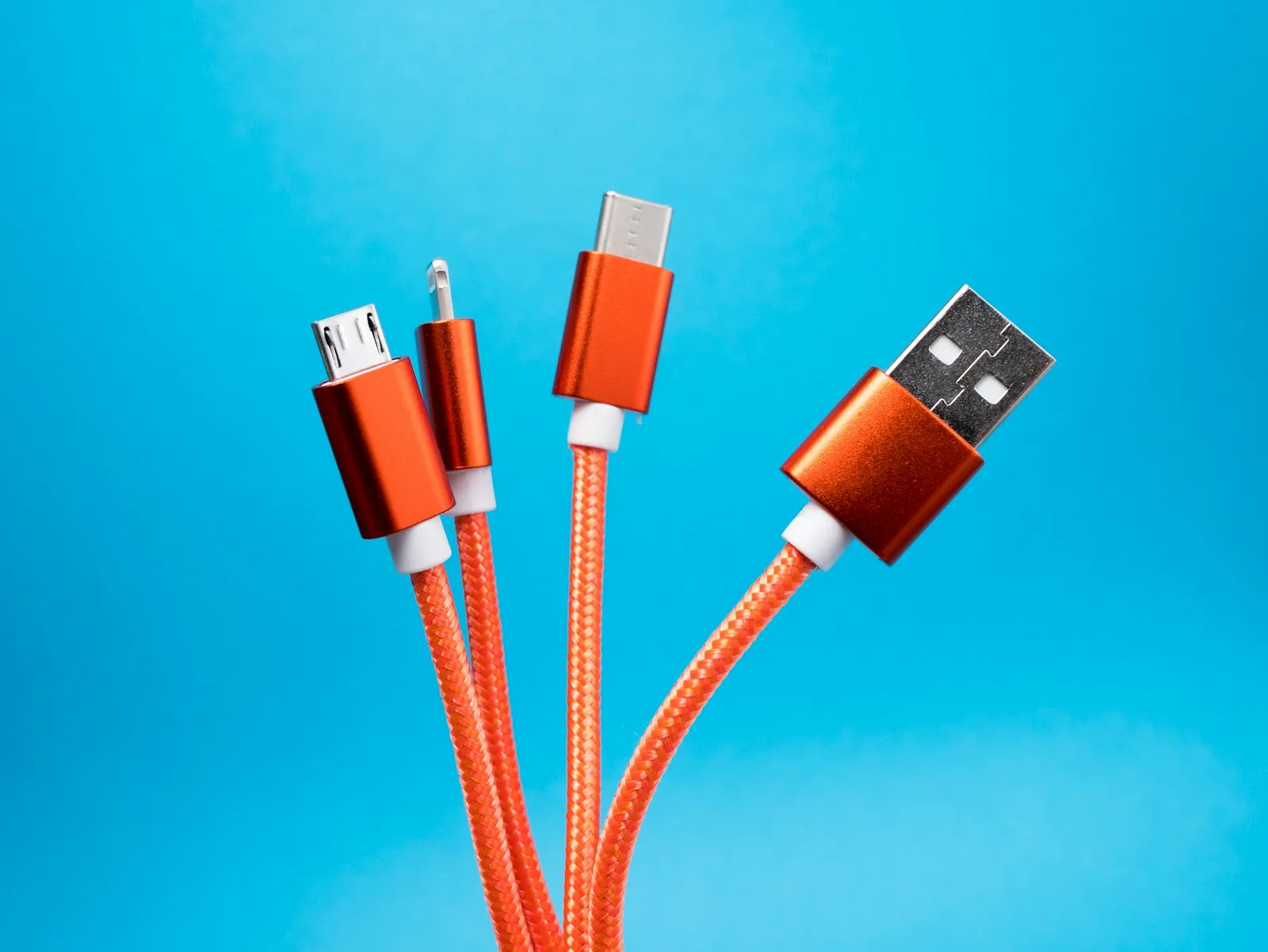 An orange braided multi-head charging cable with USB-A, USB-C, micro-USB, and Lightning connectors against a blue background.
